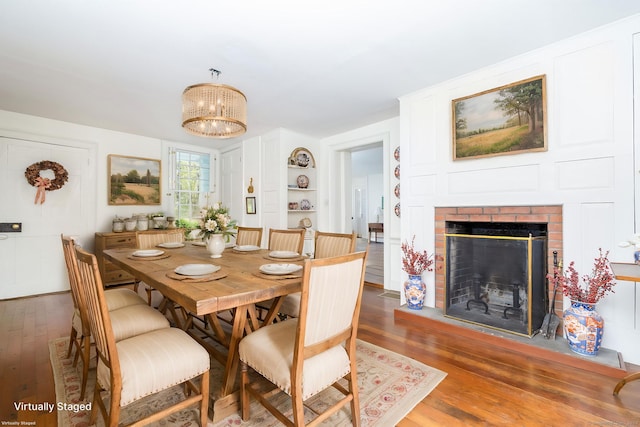 dining room with a brick fireplace, a notable chandelier, and wood finished floors