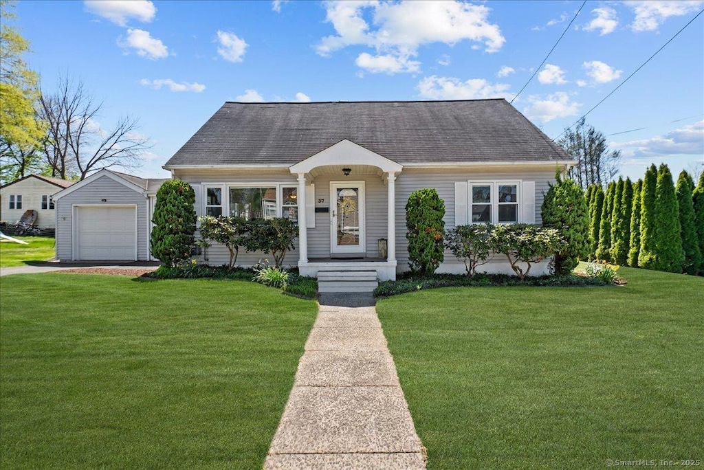 cape cod-style house featuring roof with shingles, a front yard, and a detached garage