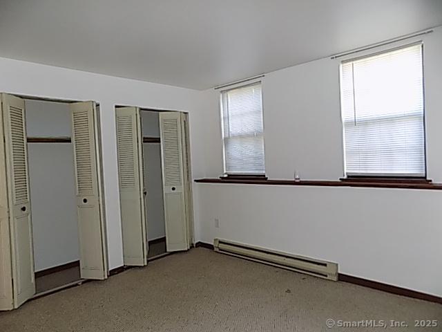 unfurnished bedroom with carpet floors, baseboards, multiple closets, and a baseboard radiator