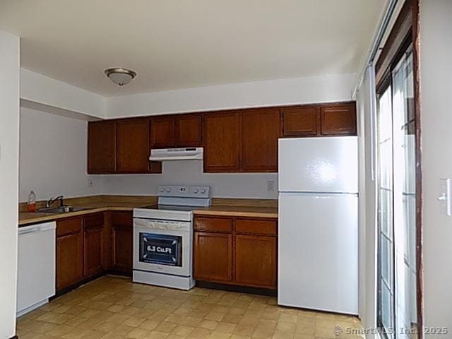 kitchen with a sink, under cabinet range hood, white appliances, and light countertops