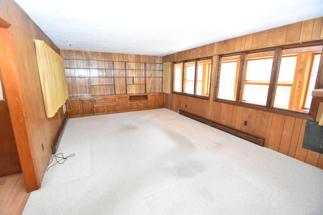 empty room featuring wooden walls, baseboard heating, and carpet