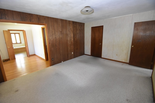 empty room with baseboards, light colored carpet, and light wood finished floors
