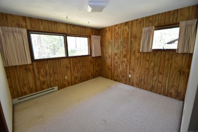 carpeted spare room with wooden walls, baseboard heating, and a healthy amount of sunlight