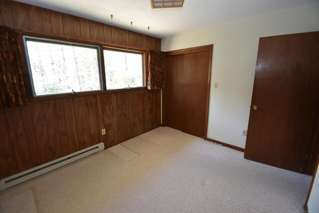 unfurnished bedroom featuring light colored carpet, wood walls, a baseboard heating unit, and a closet