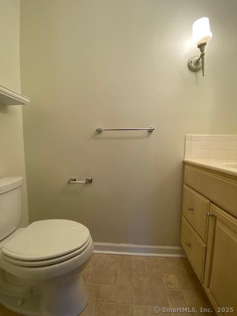 half bathroom featuring baseboards, toilet, and vanity