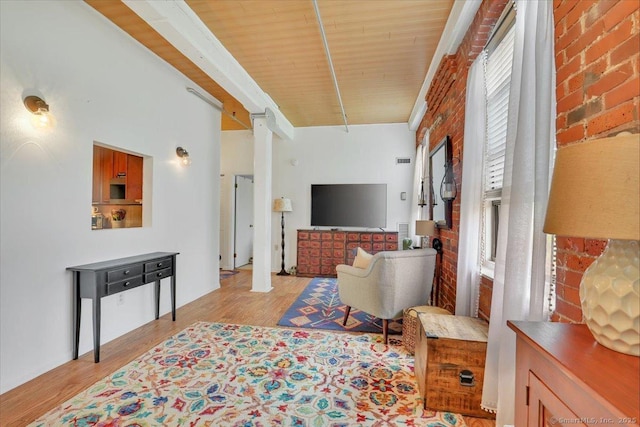 living room featuring light wood-type flooring, beamed ceiling, decorative columns, and brick wall