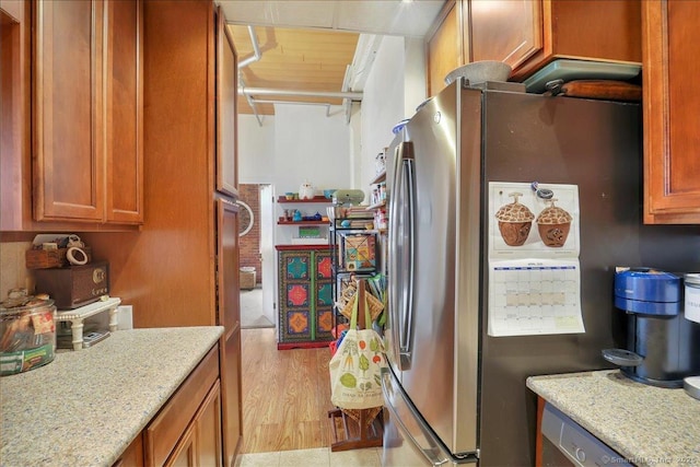 kitchen featuring brown cabinets, light stone countertops, light wood finished floors, and freestanding refrigerator