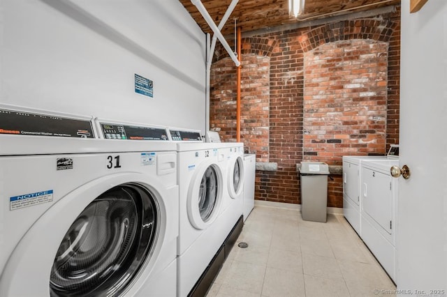 common laundry area with light tile patterned floors, washing machine and clothes dryer, and brick wall