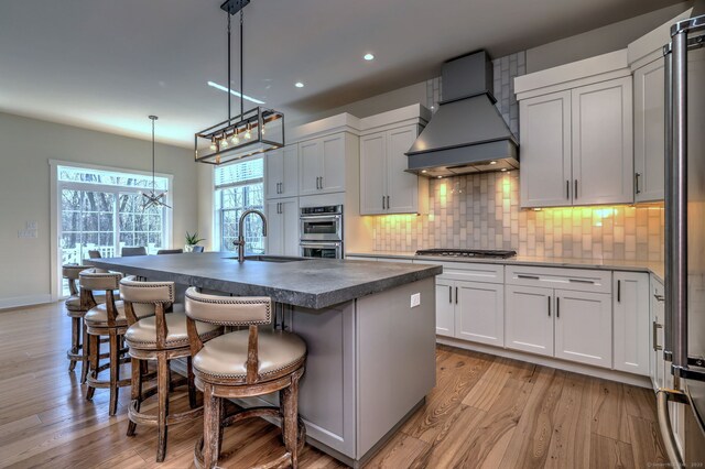kitchen featuring a sink, custom exhaust hood, a breakfast bar, backsplash, and dark countertops