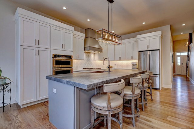 kitchen with tasteful backsplash, custom exhaust hood, light wood-style flooring, appliances with stainless steel finishes, and white cabinets