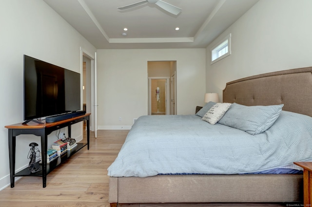 bedroom with connected bathroom, a raised ceiling, a ceiling fan, light wood-style flooring, and baseboards
