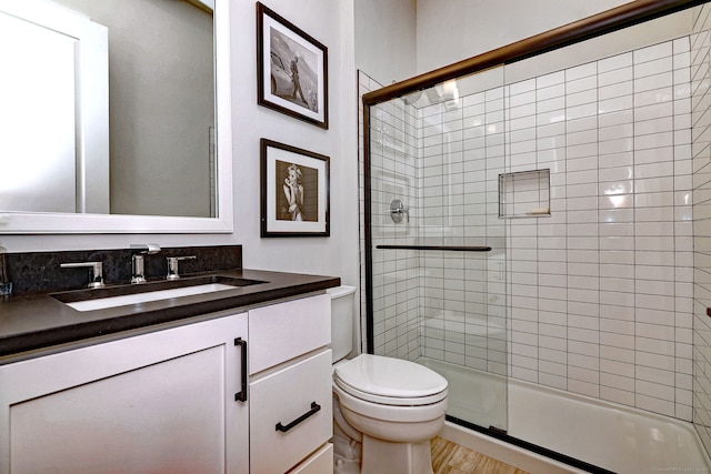 bathroom with a stall shower, toilet, wood finished floors, and vanity