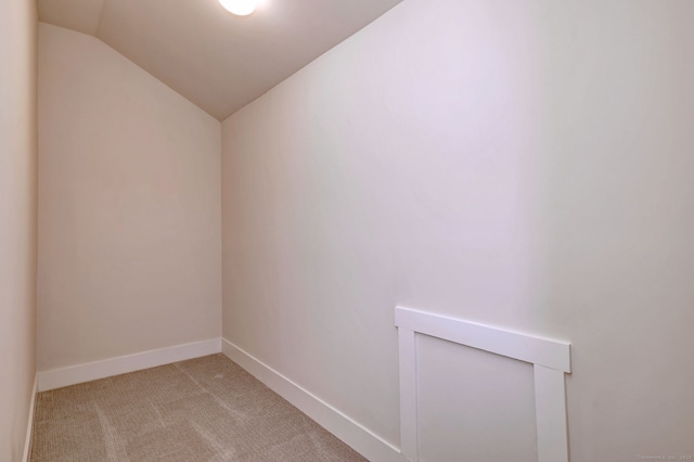 spare room featuring lofted ceiling, light colored carpet, and baseboards