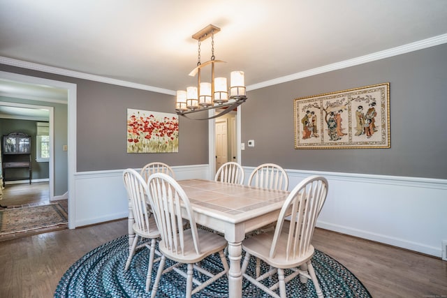 dining space with crown molding, wainscoting, wood finished floors, and a notable chandelier