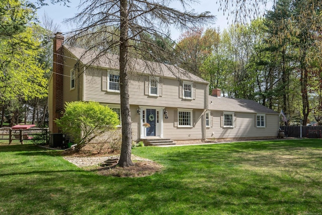back of property with fence, a chimney, a lawn, and central AC