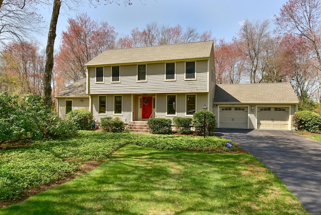 colonial house with aphalt driveway, a shingled roof, covered porch, a front yard, and an attached garage