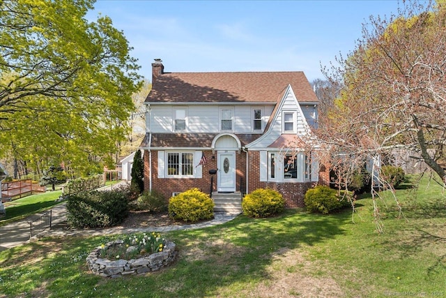 tudor house with a chimney, brick siding, fence, and a front yard