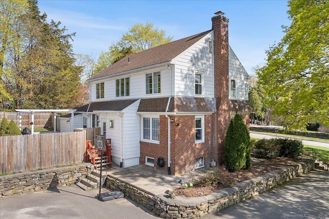 exterior space featuring fence, a chimney, a shingled roof, and brick siding