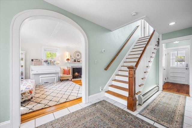 stairway with recessed lighting, arched walkways, tile patterned flooring, a warm lit fireplace, and baseboard heating