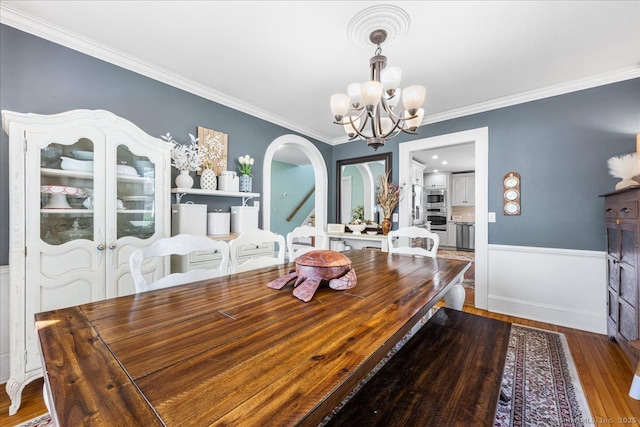dining room with a notable chandelier, ornamental molding, arched walkways, wainscoting, and wood finished floors