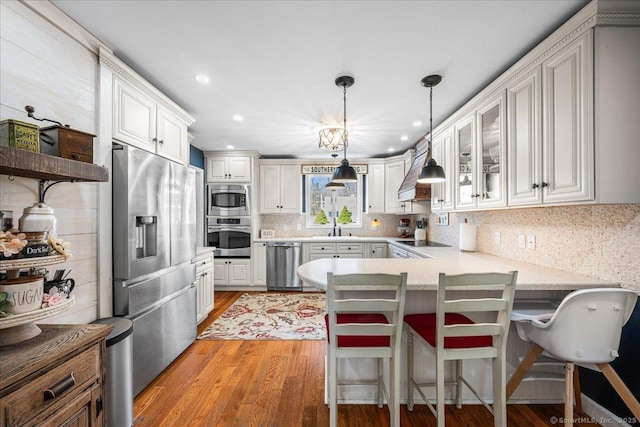 kitchen with glass insert cabinets, appliances with stainless steel finishes, decorative light fixtures, a peninsula, and backsplash