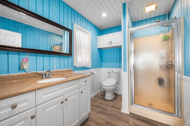 bathroom featuring a shower stall, vanity, toilet, a wainscoted wall, and wood finished floors