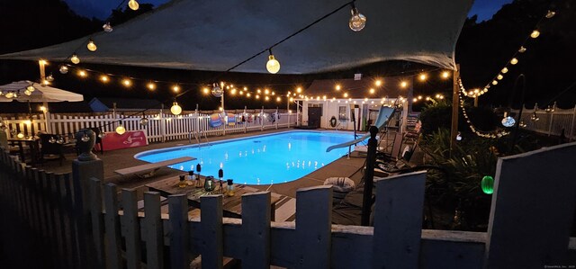 pool at night with a water slide, a diving board, fence, and a fenced in pool