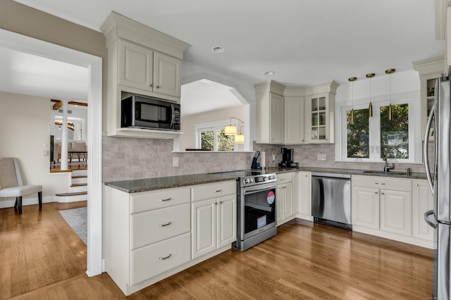 kitchen with wood finished floors, glass insert cabinets, tasteful backsplash, a sink, and stainless steel appliances