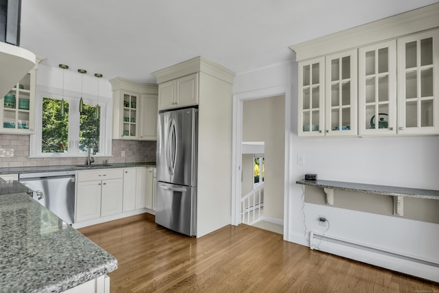 kitchen with wood finished floors, a baseboard heating unit, a sink, backsplash, and stainless steel appliances