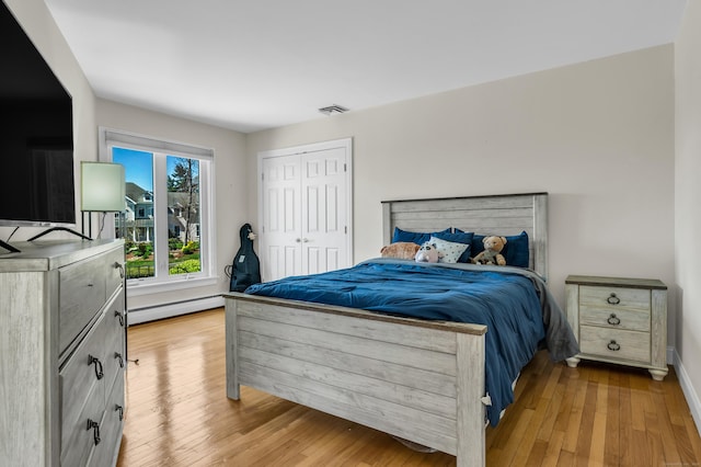 bedroom featuring visible vents, wood finished floors, baseboards, a baseboard radiator, and a closet