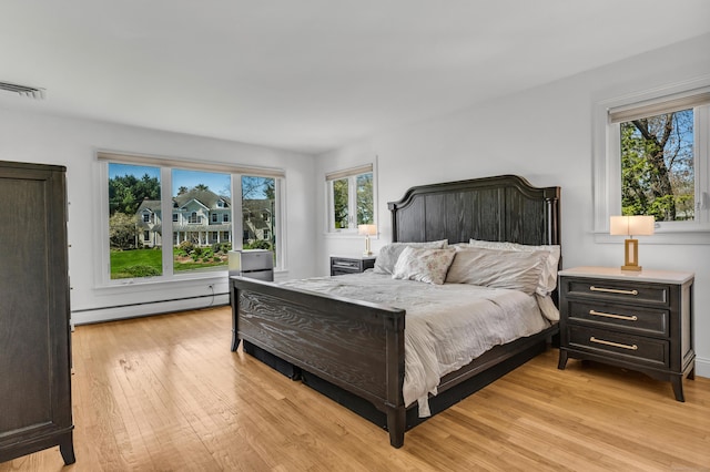 bedroom with light wood-style floors, a baseboard radiator, and multiple windows