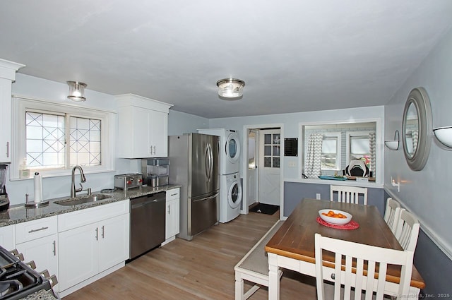 kitchen with a sink, stacked washer and clothes dryer, dishwashing machine, white cabinetry, and freestanding refrigerator