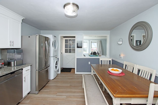 kitchen featuring white cabinetry, stainless steel appliances, stacked washing maching and dryer, light stone countertops, and light wood finished floors