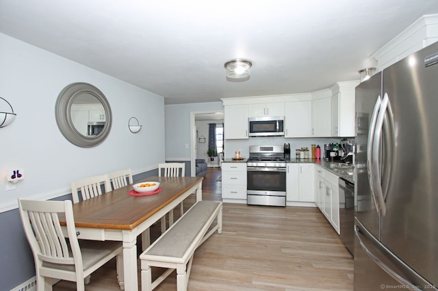 kitchen with dark countertops, white cabinetry, stainless steel appliances, and light wood-type flooring