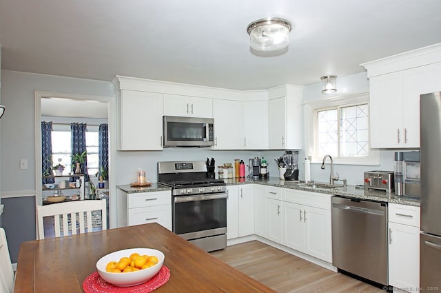 kitchen with appliances with stainless steel finishes, white cabinetry, dark stone countertops, and a sink