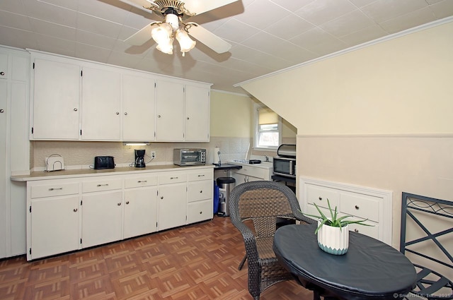 kitchen featuring ceiling fan, backsplash, light countertops, ornamental molding, and white cabinets
