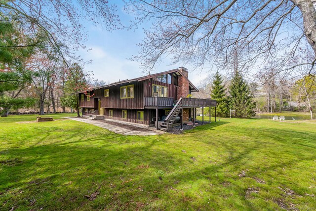rear view of house featuring a wooden deck, stairway, a chimney, a lawn, and a patio