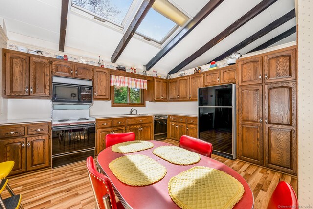 kitchen featuring light wood-style floors, light countertops, vaulted ceiling with skylight, a sink, and black appliances