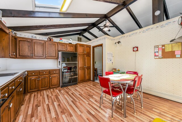 kitchen with lofted ceiling with beams, light wood finished floors, brown cabinetry, freestanding refrigerator, and a ceiling fan