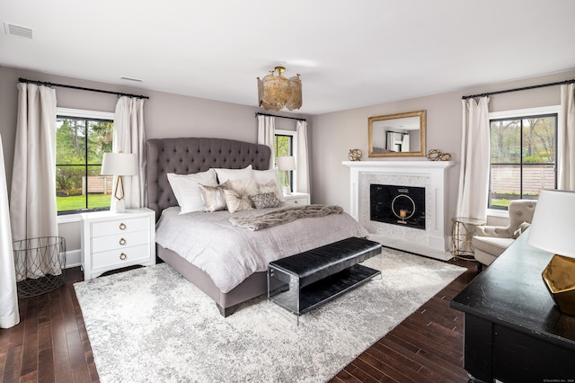 bedroom featuring a fireplace with flush hearth, dark wood-style flooring, visible vents, and multiple windows
