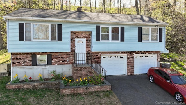 raised ranch featuring brick siding, a garage, and aphalt driveway