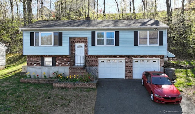split foyer home with brick siding, a garage, driveway, and a front yard
