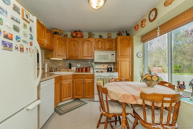 kitchen with a sink, light tile patterned floors, white appliances, tasteful backsplash, and light countertops