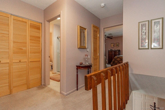 hallway with an upstairs landing, baseboards, and light carpet