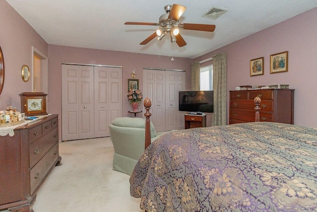 bedroom with visible vents, a ceiling fan, light colored carpet, and multiple closets