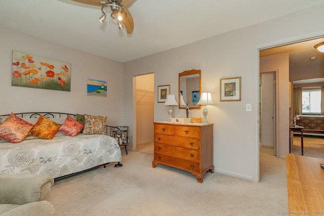 bedroom with a closet, light carpet, ceiling fan, baseboards, and a spacious closet