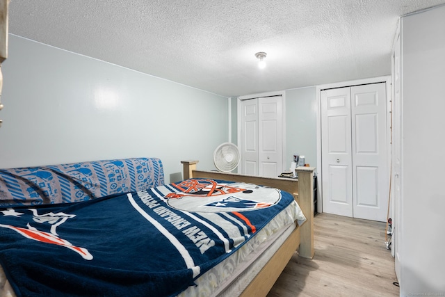 bedroom featuring a textured ceiling, light wood-style flooring, and two closets