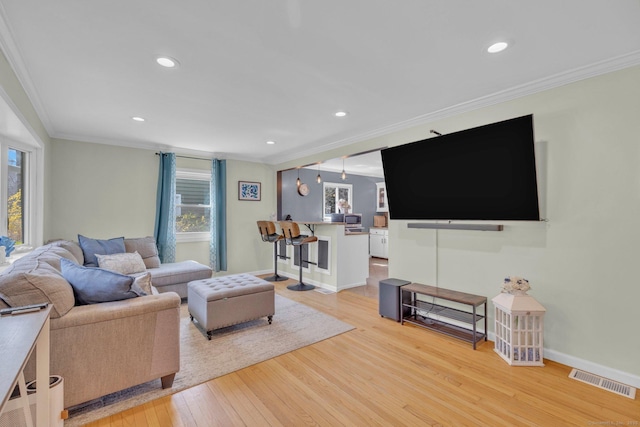 living area with visible vents, crown molding, and light wood-style floors
