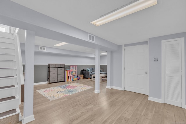 finished basement with stairs, visible vents, light wood-style flooring, and baseboards