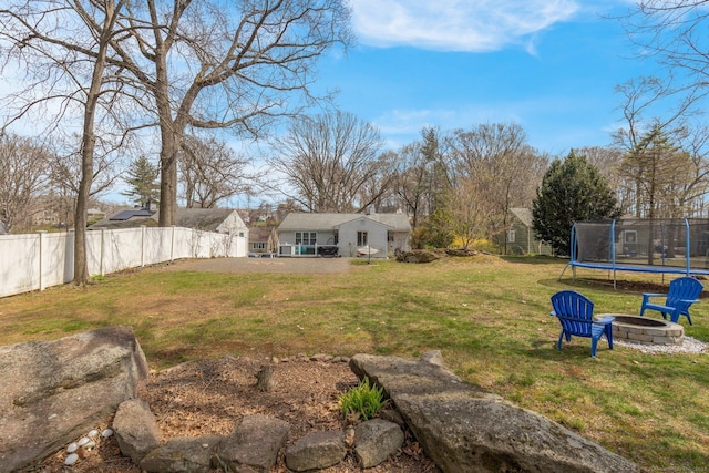 view of yard featuring a trampoline, fence, and a fire pit
